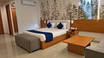 Una habitación de hotel moderna con una cama grande, una mesita de noche, una mesita de madera, un sillón gris y un ventanal con un mural de un bosque.