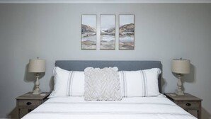 Une chambre à coucher comprenant un lit, deux tables de chevet et trois tableaux accrochés au mur.