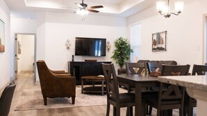 Un comedor con una mesa y sillas de madera oscura, un ventilador de techo y un televisor de pantalla plana montado en la pared.
