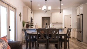 Una cocina moderna con armarios blancos, un refrigerador de acero inoxidable y una mesa de comedor con sillas oscuras.