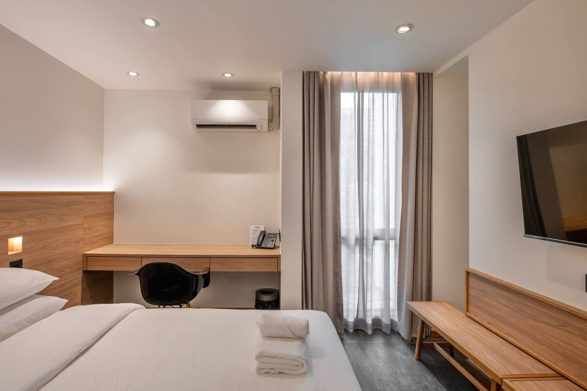 Habitación de hotel con cama, escritorio, silla, televisor y ventana con cortinas.