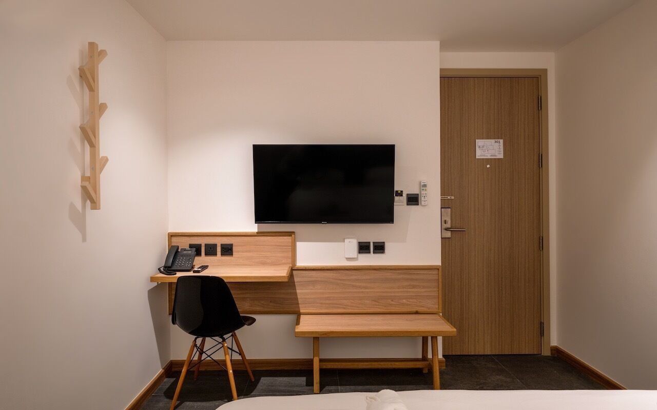 Habitación de hotel con un escritorio de madera, una silla de oficina negra, un televisor montado en la pared y una puerta con un cartel.