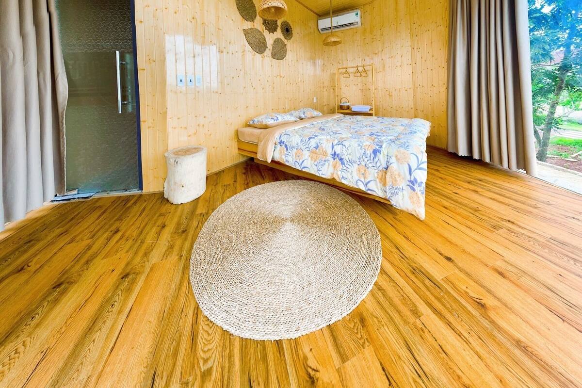 Quarto espaçoso com uma cama grande, piso de madeira e vista para o verde lá fora.