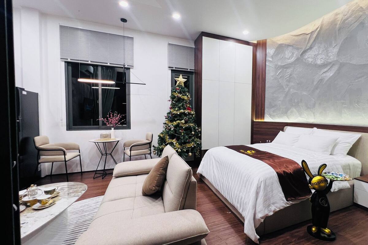 Um quarto moderno com uma cama, uma mesinha, um pinheiro de Natal e um sofá.