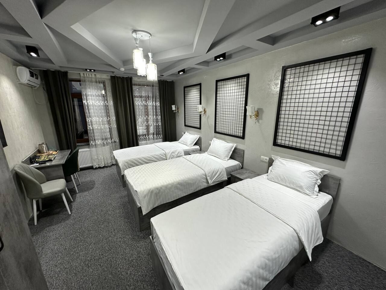 Habitación de hotel con tres camas individuales, un escritorio con silla y una mesita con tetera.