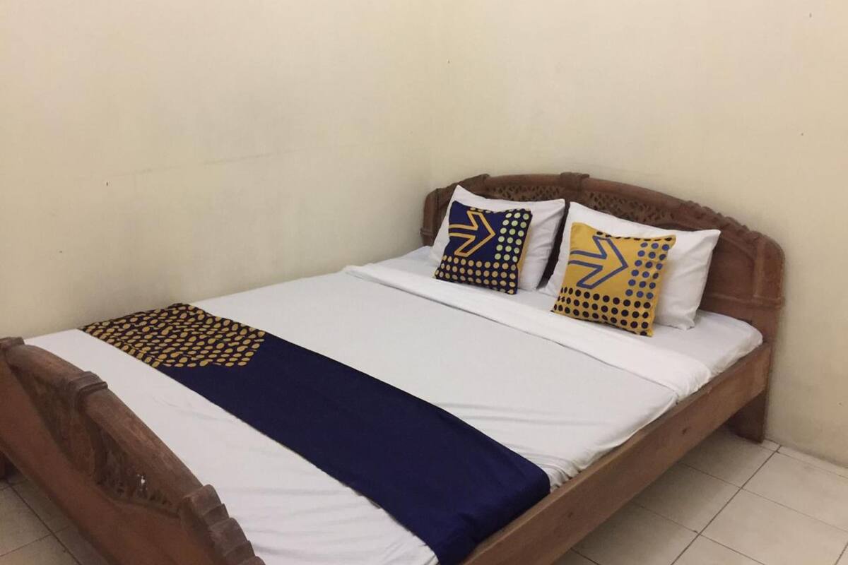 A single bed with a wooden headboard, white bedding, and two decorative pillows with geometric patterns.