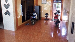 Um corredor com piso ladrilhado, uma scooter estacionada perto de uma porta, e uma motocicleta ao fundo.