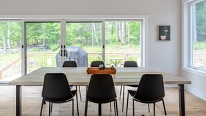 A dining area with a large table, four chairs, and a grill outside. - Airy Tree Canopy Home w/ Creek Views & Family Suite (Sparrow Bush)