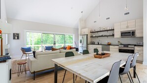 A modern kitchen with a dining area, large windows, and a view of greenery. - Airy Tree Canopy Home w/ Creek Views & Family Suite (Sparrow Bush)
