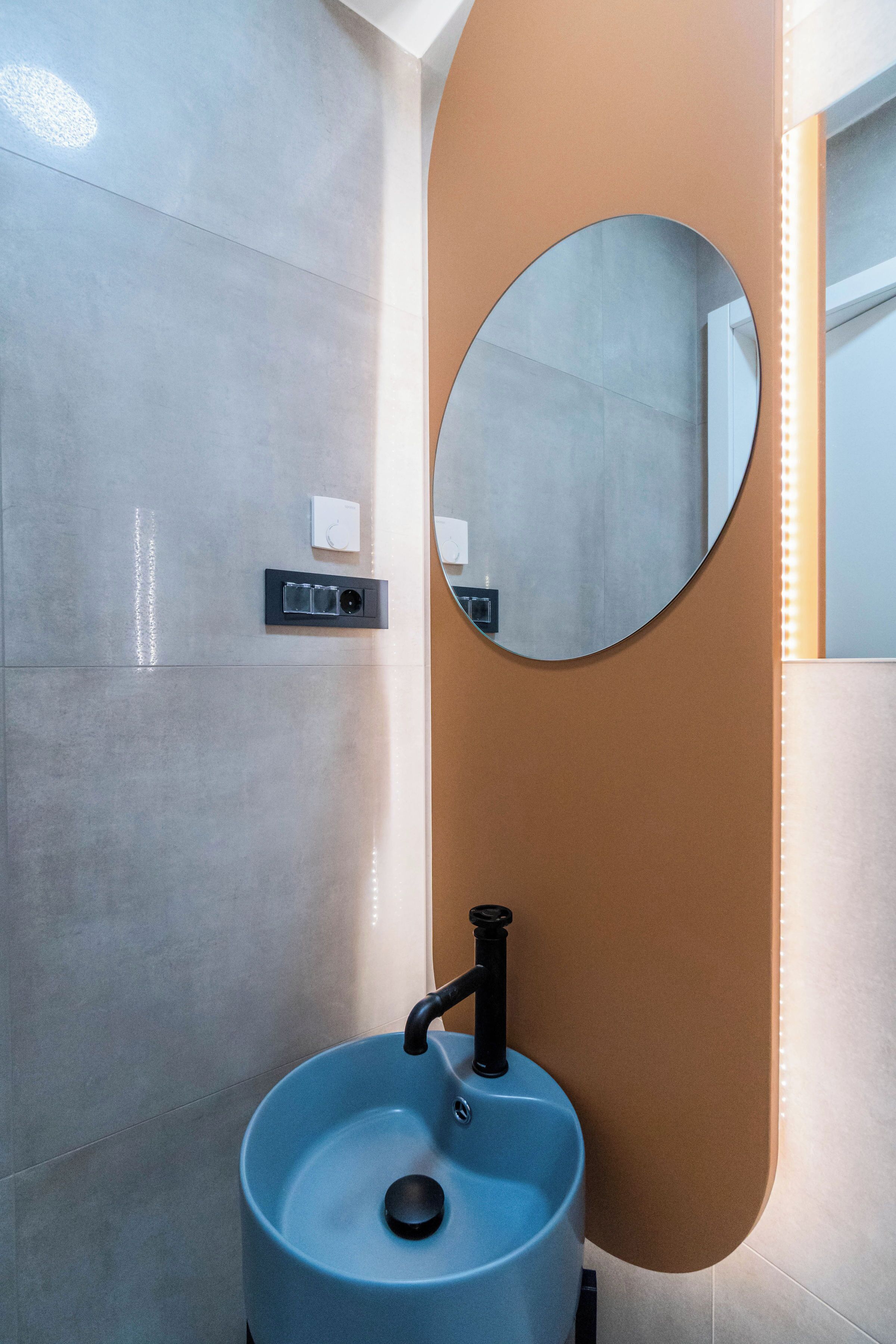 A bathroom with a blue sink, a round mirror, and a wall-mounted light fixture.