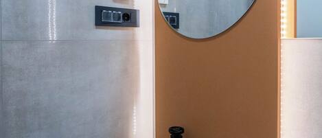 A bathroom with a blue sink, a round mirror, and a wall-mounted light fixture.