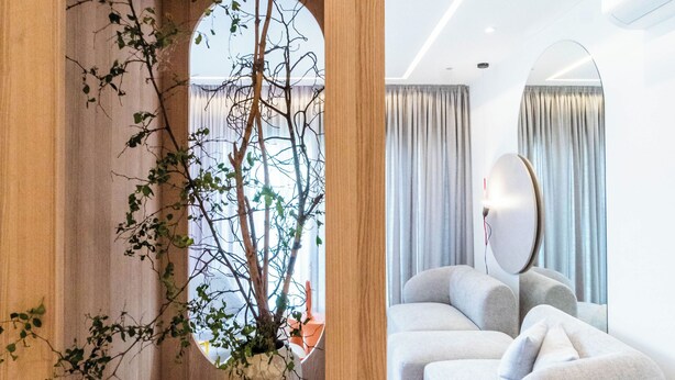 Ein modernes Interieur mit einem hölzernen Bogen, der in einen Sitzbereich mit einem grauen Sofa und einem großen Spiegel führt.