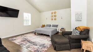 Een moderne slaapkamer met een bed, een grijze bank, een houten bijzettafeltje en een plafondventilator.