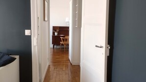 A hallway with wooden flooring leading to a room with a bed and a desk. - 1 Bedroom Apartment in Paris (Paris)