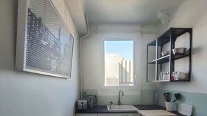 A compact kitchen with a window, a sink, a countertop, and a small table with cups. - 1 Bedroom Apartment in Paris (Paris)