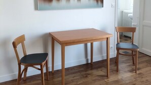 A room with a wooden table and two chairs, a large abstract painting on the wall, and a radiator in the background. - 1 Bedroom Apartment in Paris (Paris)