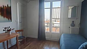 A bedroom with a wooden floor, a bed, a desk with a chair, a window with curtains, and a painting on the wall. - 1 Bedroom Apartment in Paris (Paris)