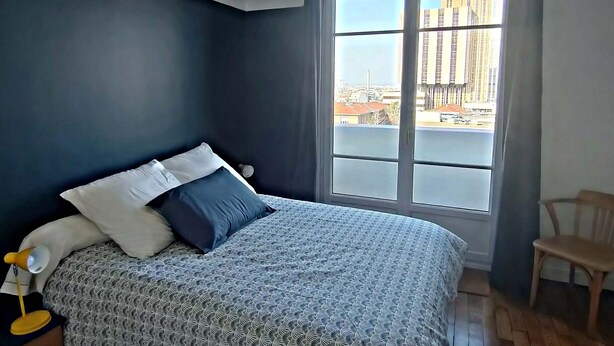 A bedroom with a large bed, a nightstand, a chair, and a window with curtains. - 1 Bedroom Apartment in Paris (Paris)