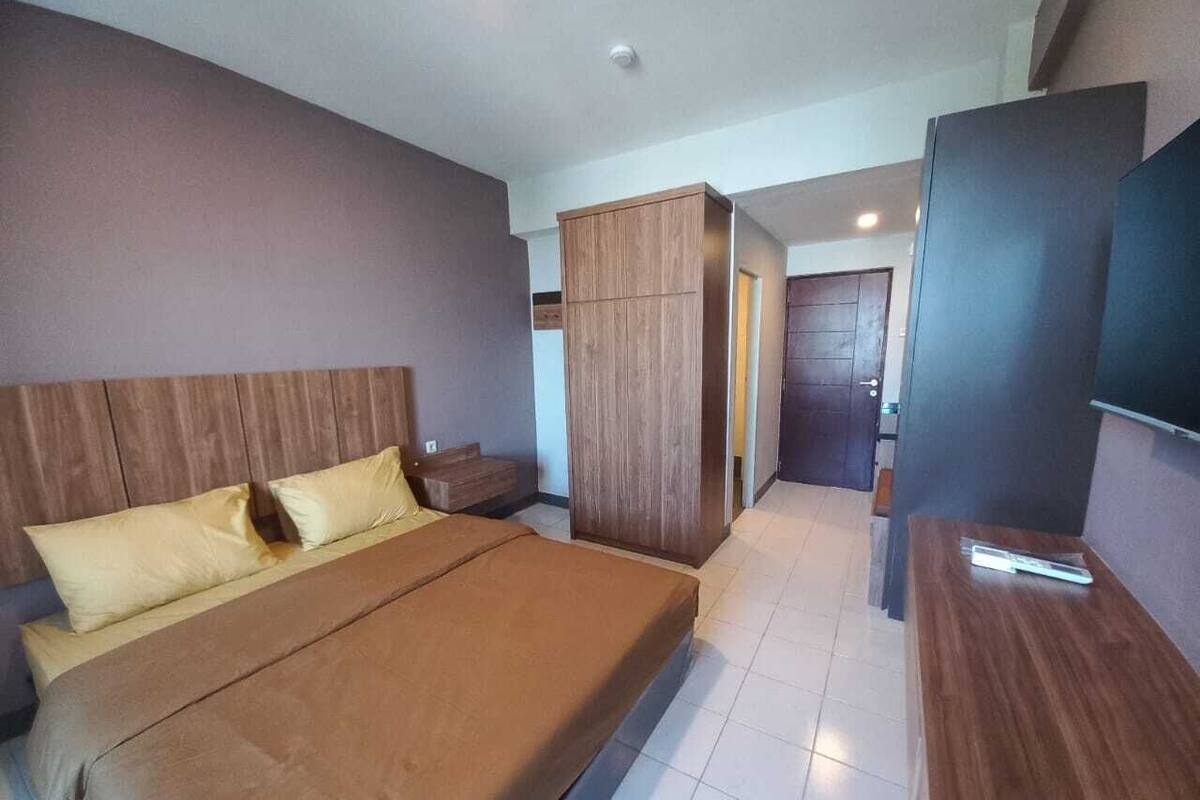 Ein modernes Hotelzimmer mit einem großen Bett, einem Holzschrank und einem Flachbildfernseher.
