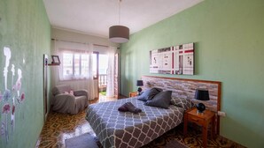 Een slaapkamer met een bed, twee nachtkastjes, een hanglamp, een raam met gordijnen en een wand met een schilderij.