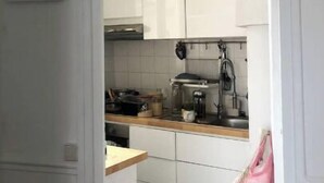 A kitchen with white cabinets, a hanging light fixture, and a countertop with various kitchen items. - Montreuil City, Artists (Montreuil)