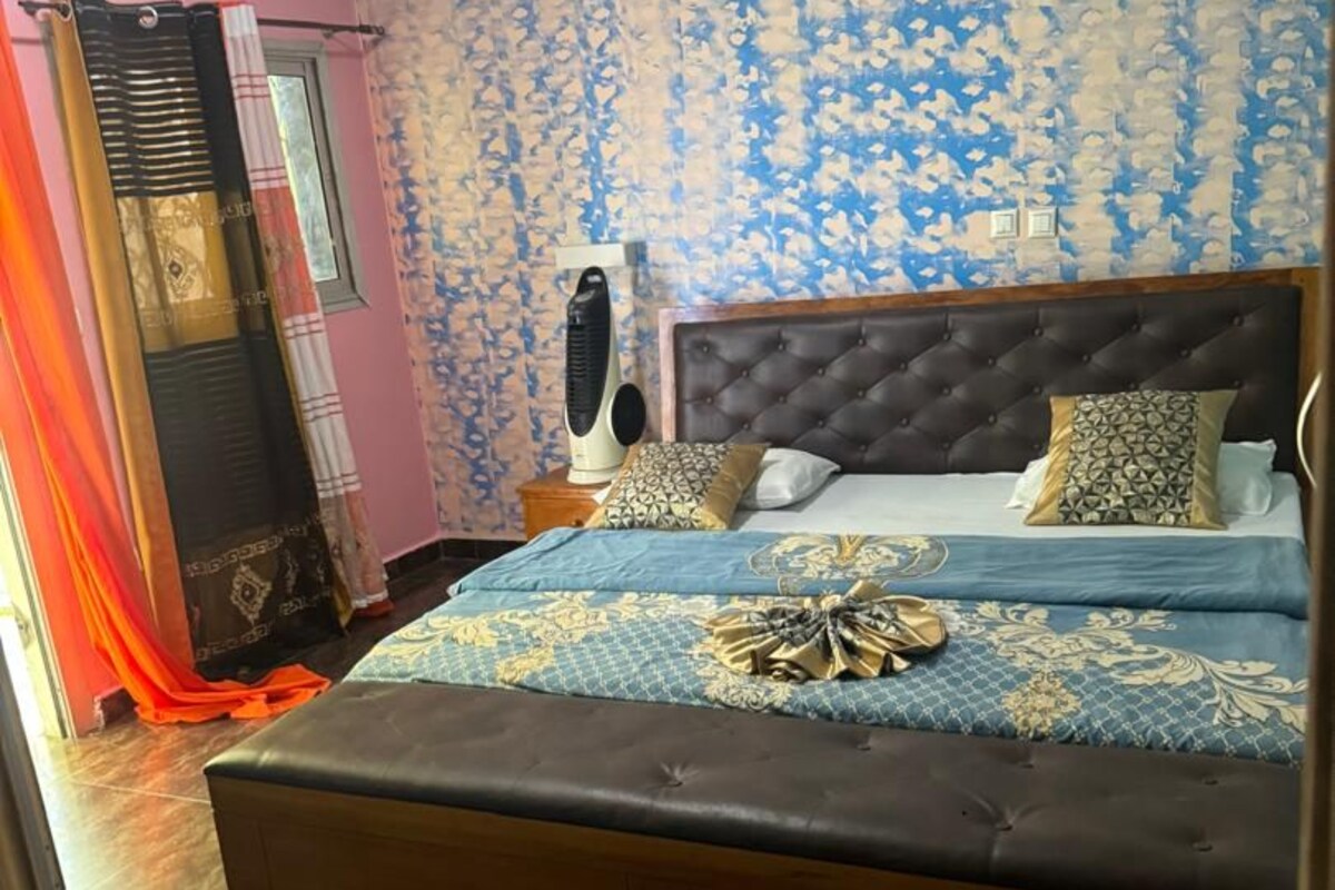 Een slaapkamer met een bed, nachtkastje, wandheater en een raam met gordijnen.