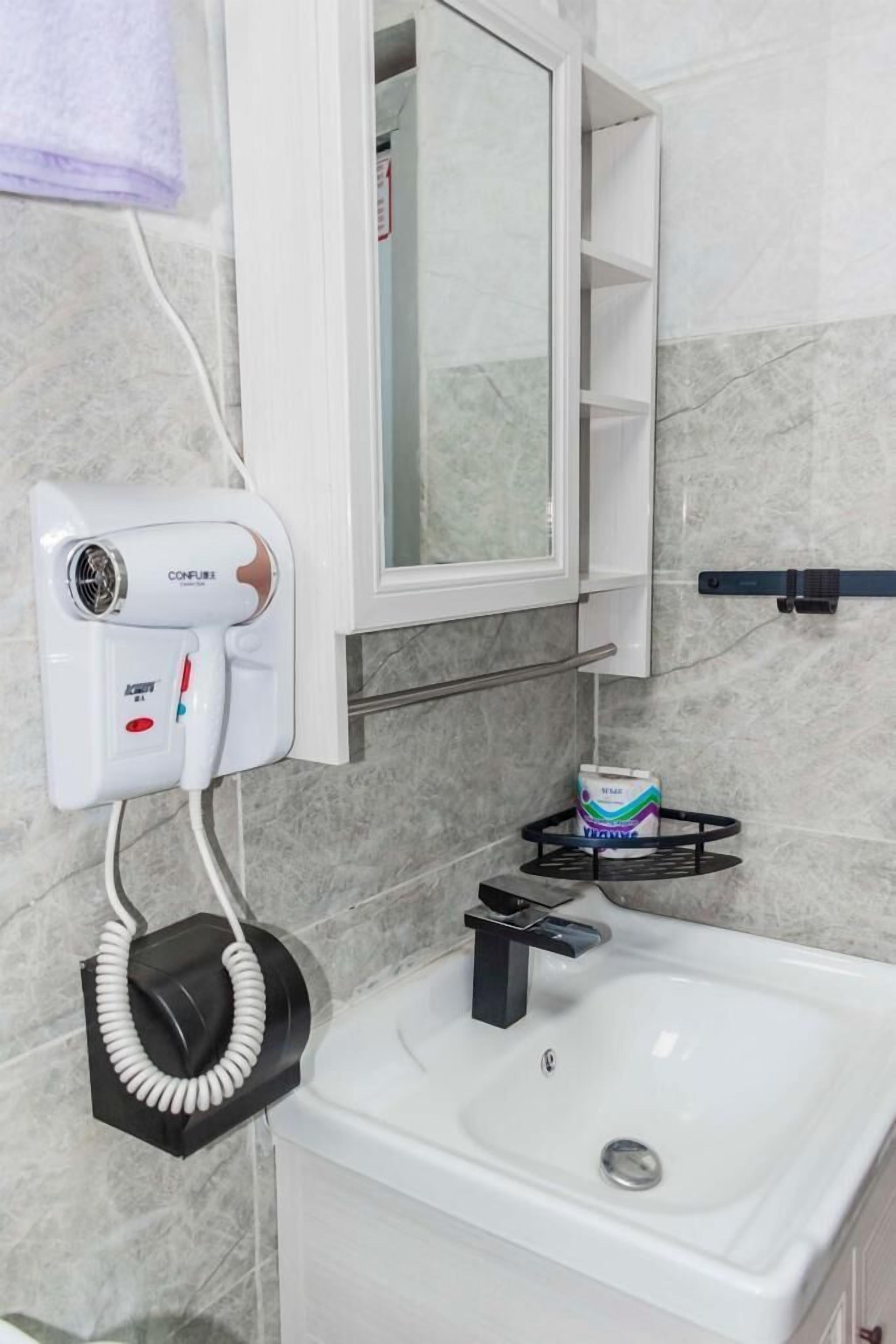 A bathroom with a white sink, a towel rack, a mirror, a hairdryer, and a soap dispenser.