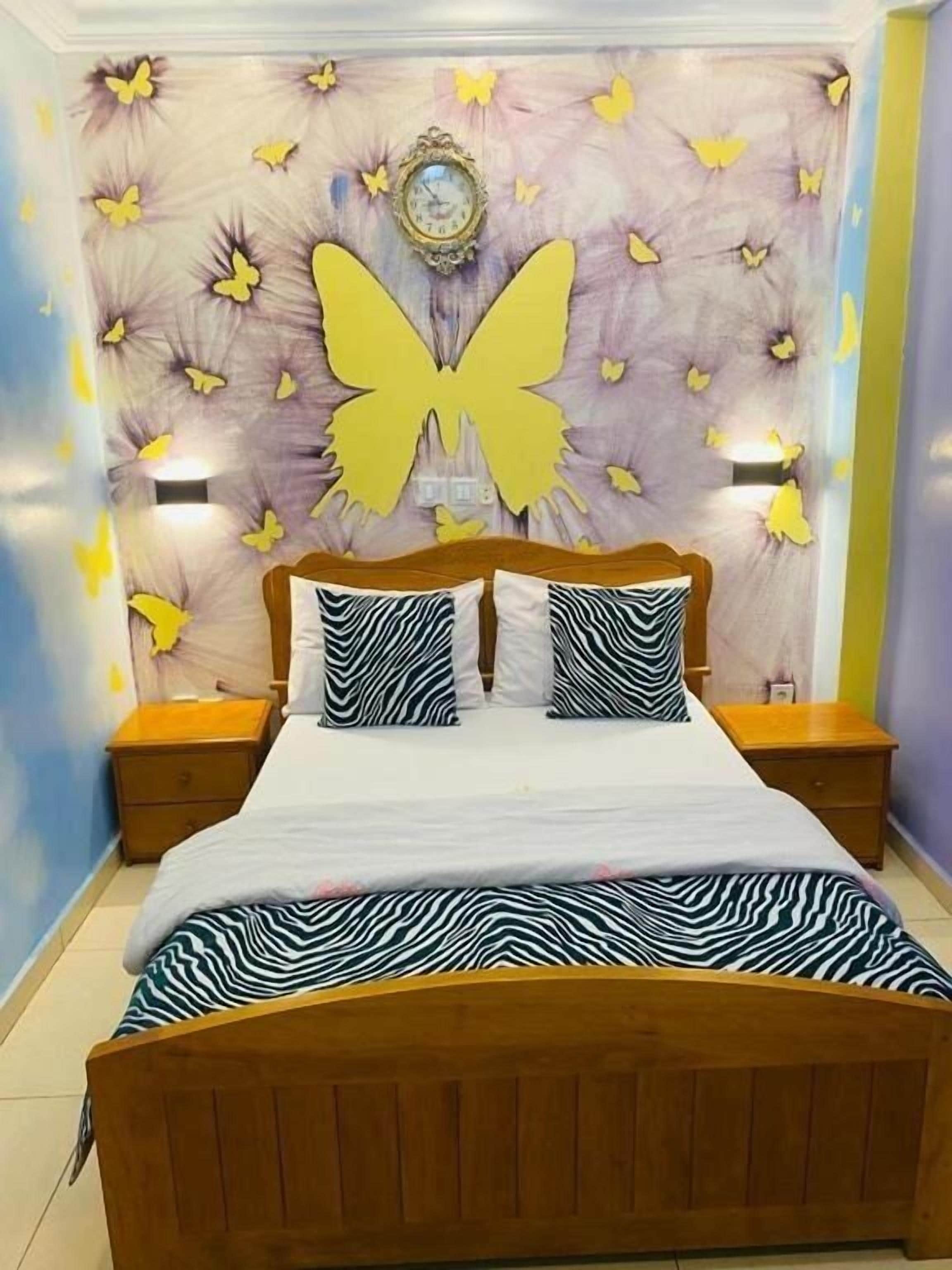 A bedroom with a large butterfly wall decoration, a bed with zebra-patterned bedding, and two bedside tables.