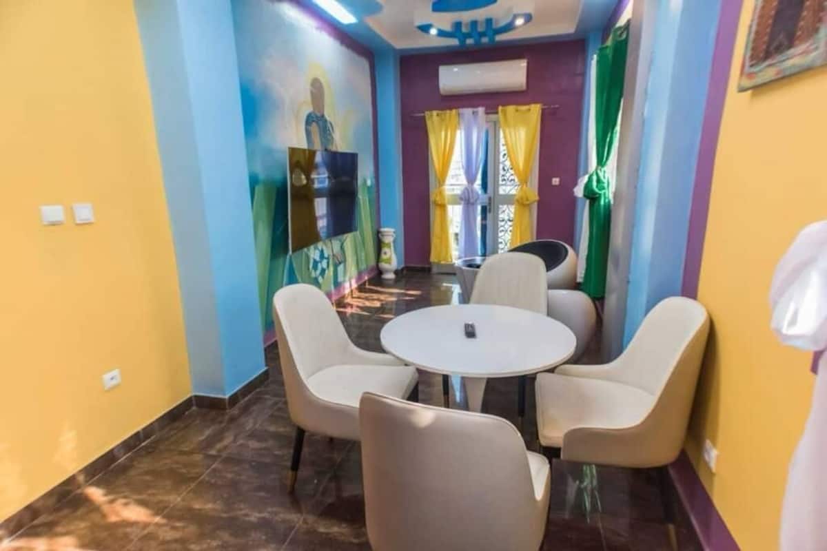 Un couloir avec une table ronde et quatre chaises, qui mène à une pièce dont un mur est décoré d’une fresque.