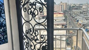 Ein Balkon mit schmiedeeisernem Geländer, Fliesenboden und Blick auf eine Stadtansicht.