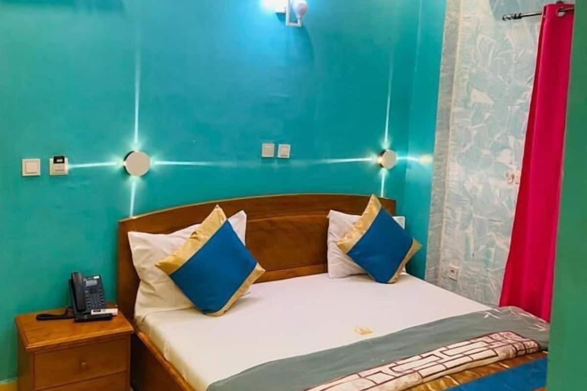 Une chambre à coucher avec un lit en bois, une literie bleue et blanche, une table de chevet avec un téléphone et un luminaire fixé au mur.