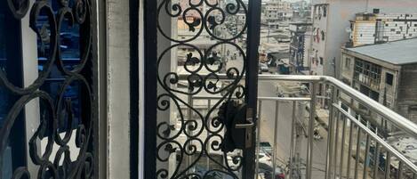A balcony with a decorative metal gate, a view of the cityscape, and a tiled floor.
