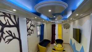 Ein Zimmer mit modernem Deckenstil, einem an der Wand montierten Fernseher und einer Sitzecke mit gelben Stühlen.