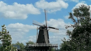 A traditional windmill with a modern structure at its base, situated by a body of water with surrounding greenery. - Tinyhaus "carpe Diem" (Dirkshorn)