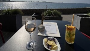 Un tavolo con un menu, un bicchiere di vino bianco, un cocktail e un piccolo piatto di patatine e frutta in un ristorante sul mare.