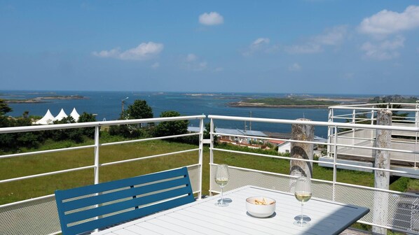 A table with a bowl of food and two glasses of wine, overlooking a coastal view with a clear sky.