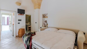 A bedroom with a bed, a television mounted on the wall, a door leading to a bathroom, and a wicker basket on the floor. - Superior Apt - Corte dei Mesci - By Just Houses SRL (Specchia)