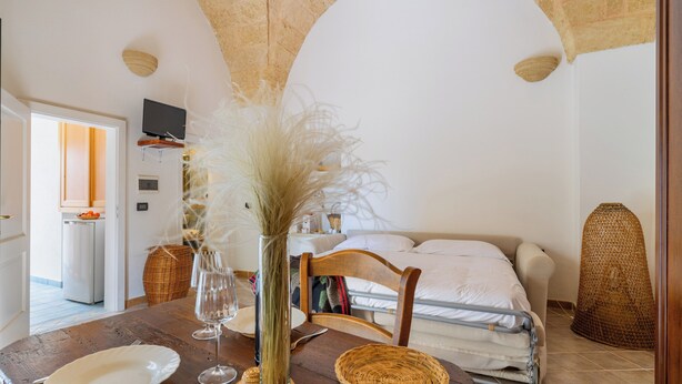 A dining table with a vase of dried plants, a plate, and a wine glass. - Superior Apt - Corte dei Mesci - By Just Houses SRL (Specchia)
