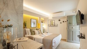 Habitación de hotel con pared de mármol, cama con manta color beige, mesita de noche con lámpara y televisor montado en la pared.