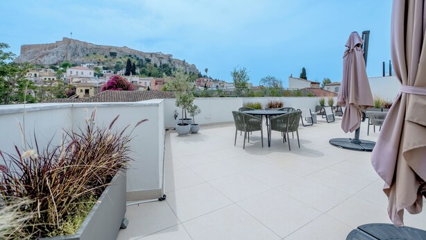 A rooftop terrace with outdoor seating, potted plants, and a view of a historic hilltop fortress.