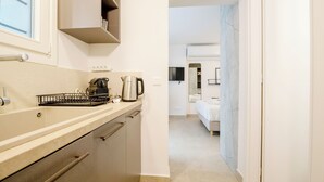 A modern kitchen with a countertop, kettle, and dish rack. A hallway leads to a bedroom with a bed and a wardrobe.