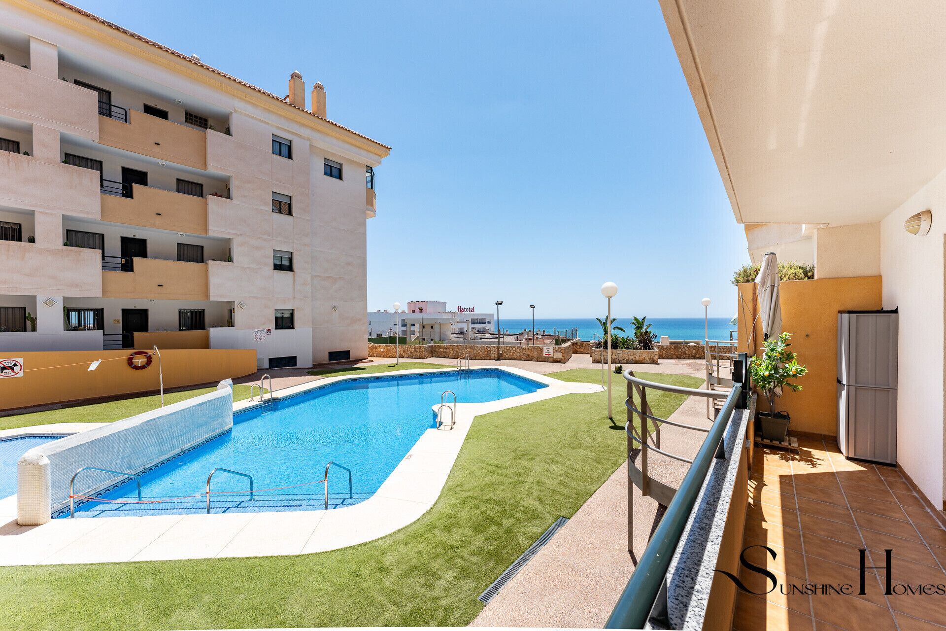 A swimming pool with a view of the sea, a balcony with a railing, and a building with multiple balconies.