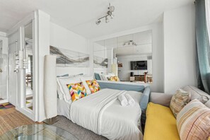 Relax in a spacious room with a large bed, sofa, and desk, featuring a large mirror and modern decor.