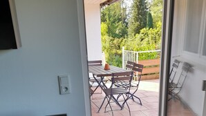 Een kamer met een schuifglazen deur die uitkomt op een terras met een tafel en stoelen.