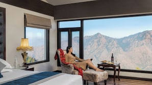 Habitación de hotel con una cama grande, una silla, una mesita y vistas a montañas.