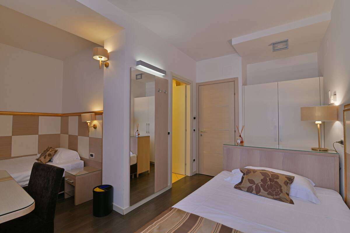 A hotel room with a bed, a desk, a chair, a mirror, and a wardrobe.