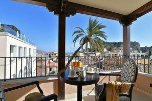 Ein Balkon mit Tisch für zwei Personen, mit Blick auf eine Stadtlandschaft mit Gebäuden und einer Palme.
