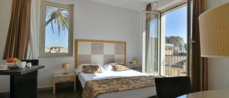 A hotel room with a bed, bedside table, lamp, and a view of the city through a large window.