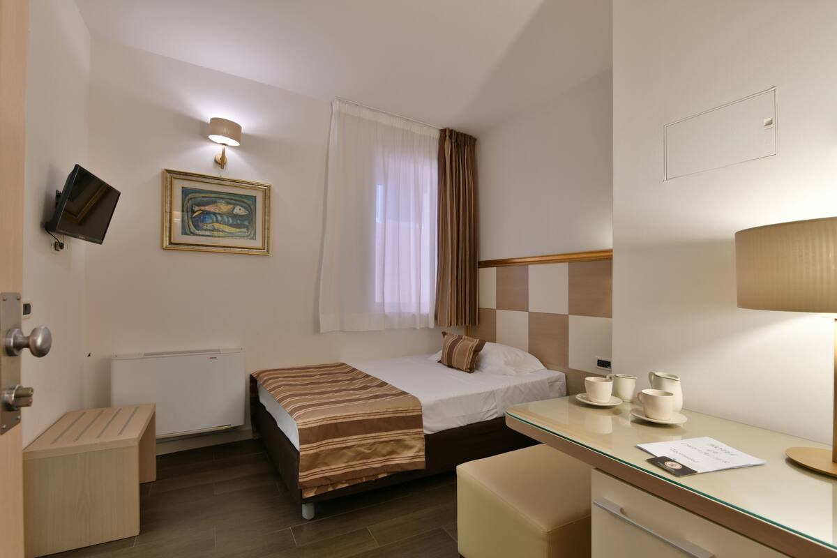 A hotel room with a bed, bedside table, lamp, and a painting on the wall.