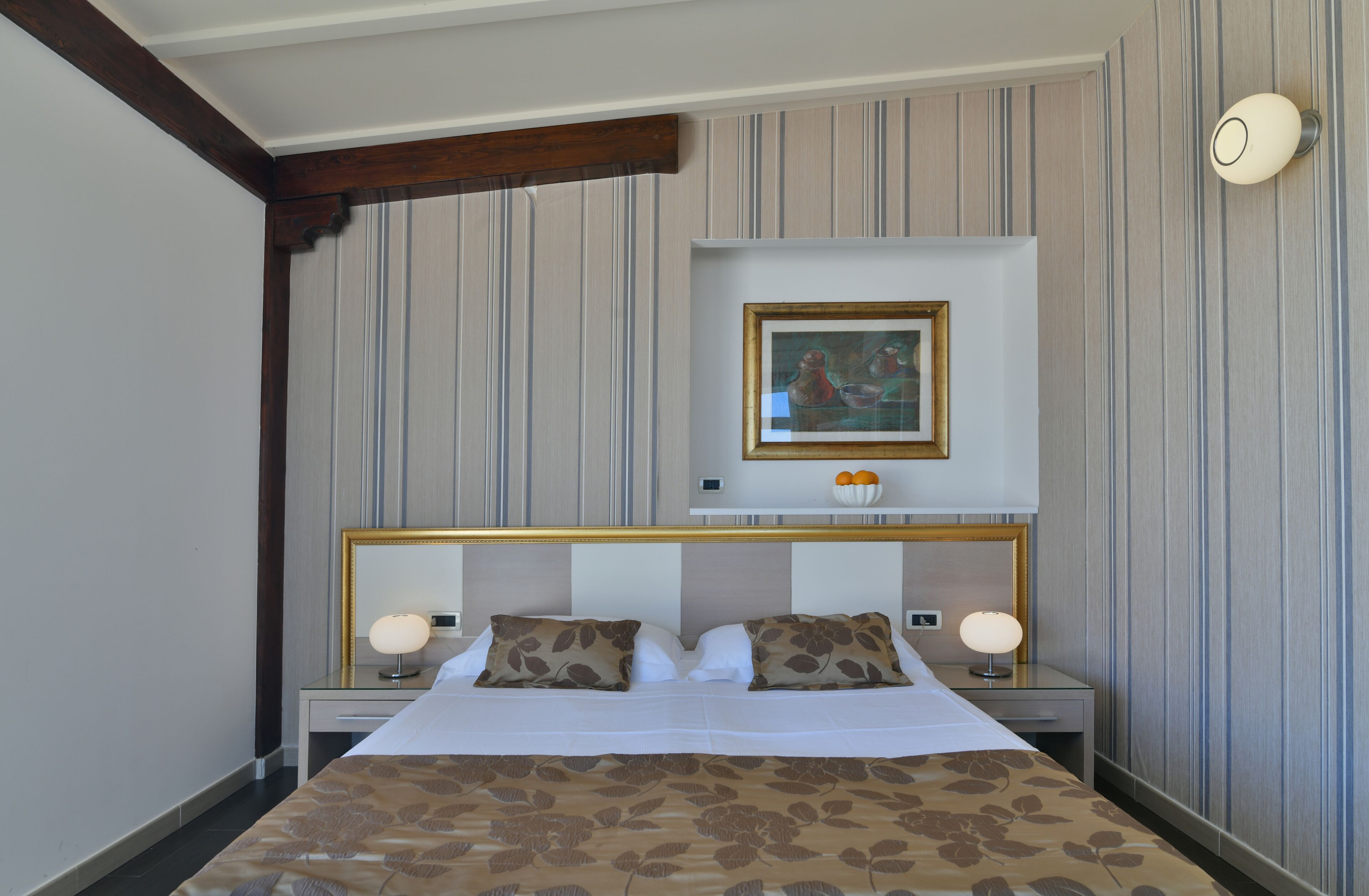 Quarto de hotel com uma cama grande, duas mesas de cabeceira, uma luminária de parede e um quadro emoldurado sobre a cama.